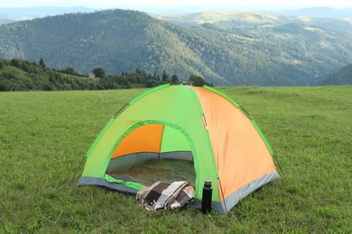 Tent, thermos and blanket on green grass in mountains