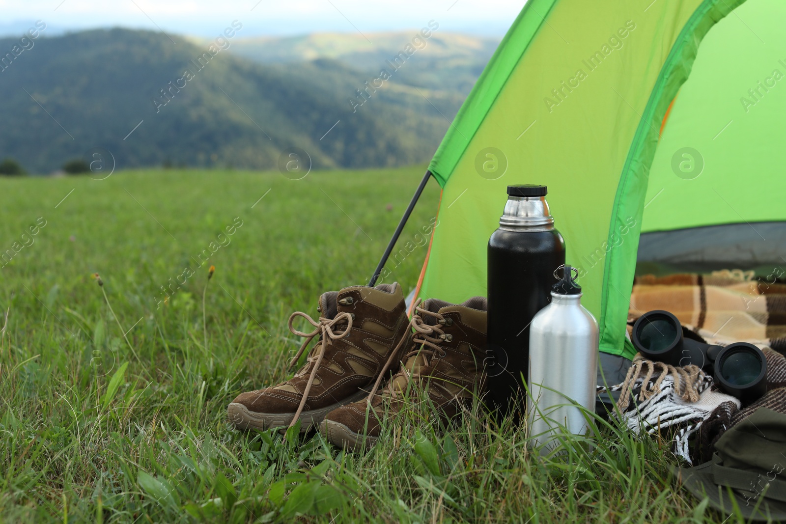 Photo of Tent and camping equipment on green grass in mountains, space for text