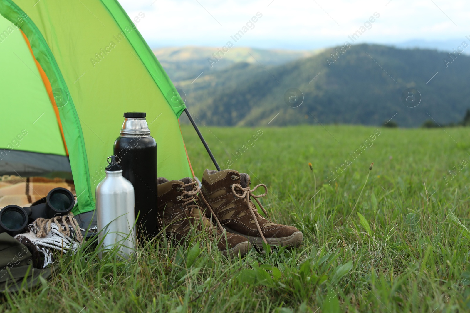 Photo of Tent and camping equipment on green grass in mountains, space for text