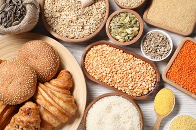 Photo of Different types of cereals, seeds, bread and legumes on white wooden table, flat lay