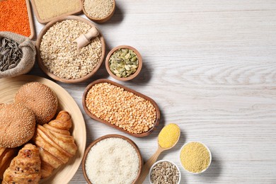 Photo of Different types of cereals, seeds, bread and legumes on white wooden table, flat lay. Space for text