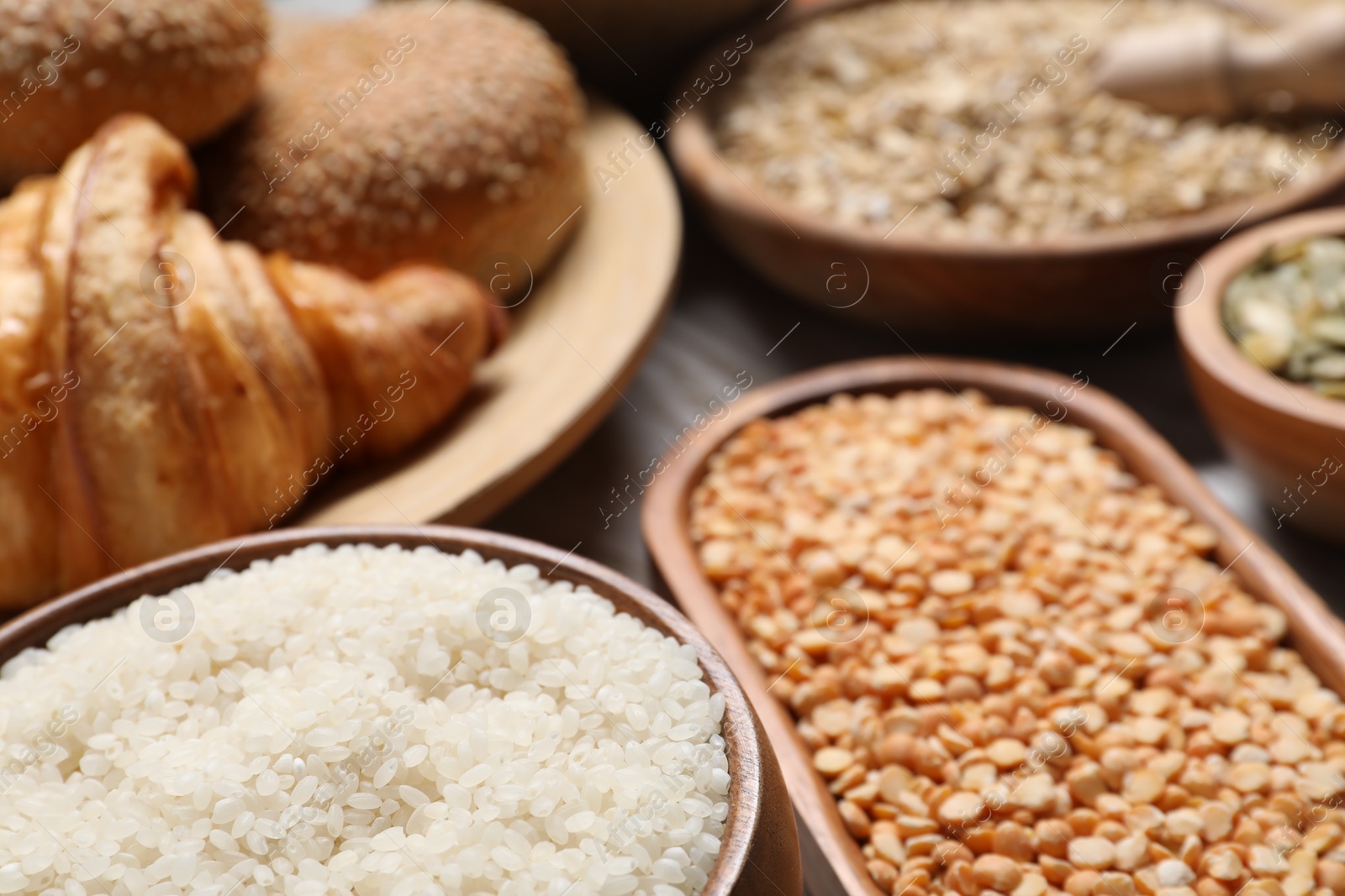 Photo of Different types of cereals, seeds, bread and legumes on wooden table, closeup