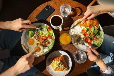 Photo of Couple having tasty breakfast at wooden table in cafe, top view