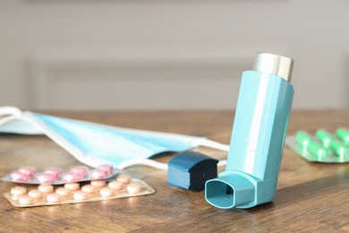 Photo of Inhaler, medical mask and pills on wooden table indoors, closeup. Asthma treatment