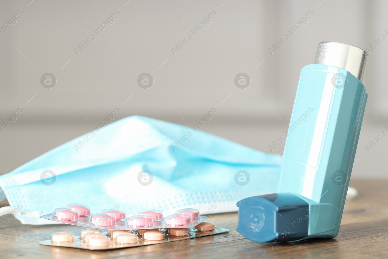 Photo of Inhaler, medical mask and pills on wooden table indoors, closeup. Asthma treatment