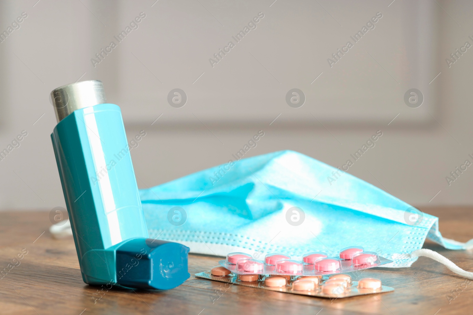 Photo of Inhaler, medical mask and pills on wooden table indoors, closeup. Asthma treatment