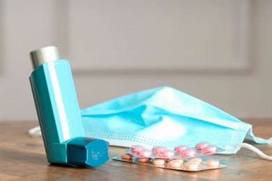 Photo of Inhaler, medical mask and pills on wooden table indoors, closeup. Asthma treatment