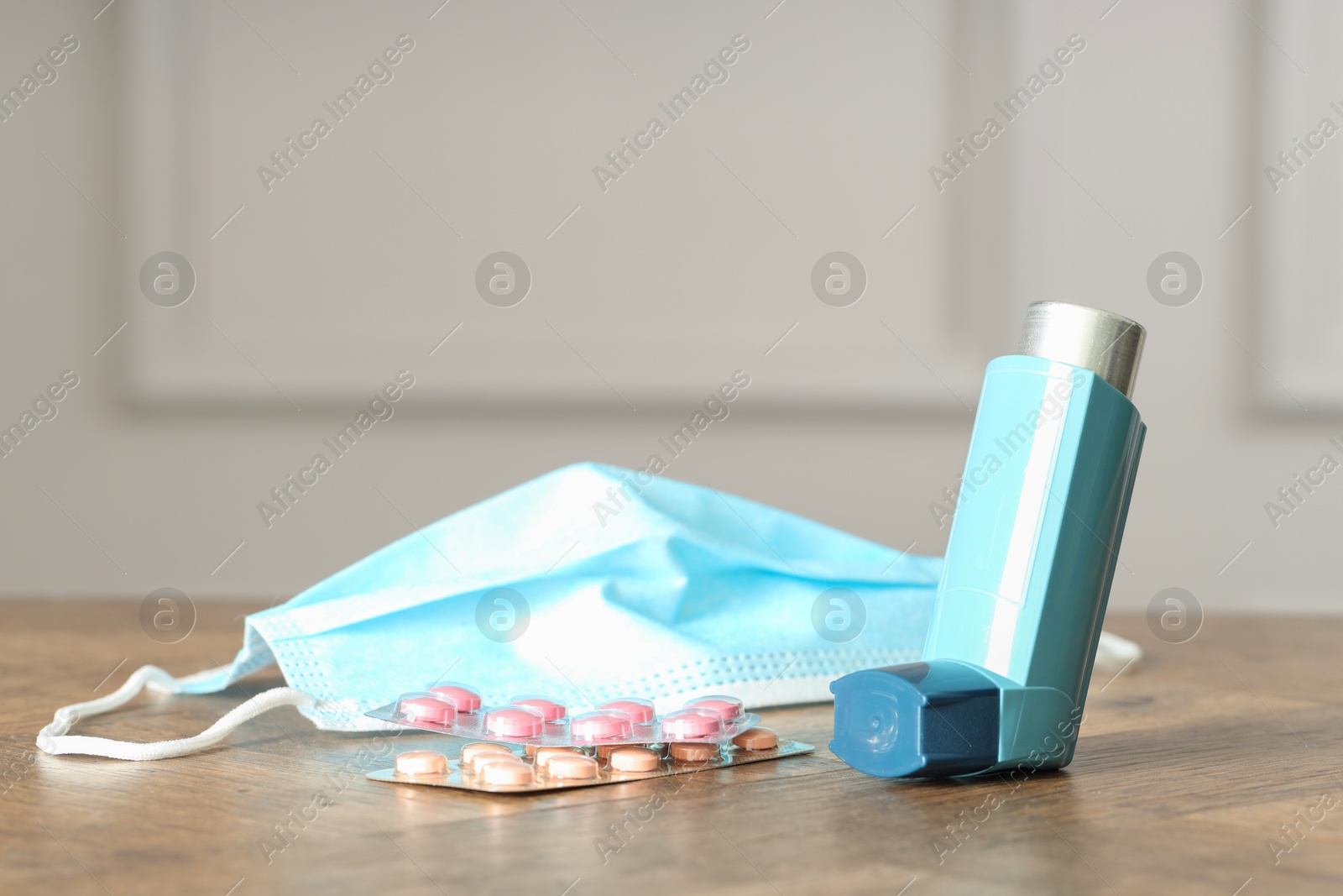 Photo of Inhaler, medical mask and pills on wooden table indoors, closeup. Asthma treatment