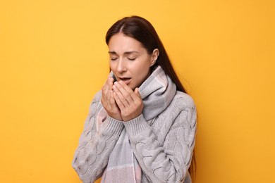 Sick woman sneezing on orange background. Cold symptoms