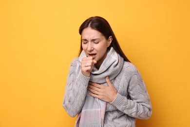 Sick woman coughing on orange background. Cold symptoms