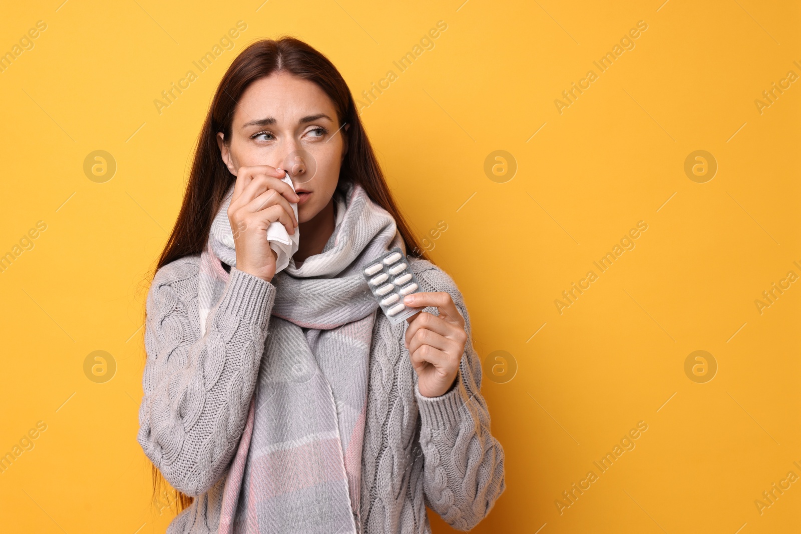 Photo of Sick woman with tissue and pills on orange background, space for text. Cold symptoms