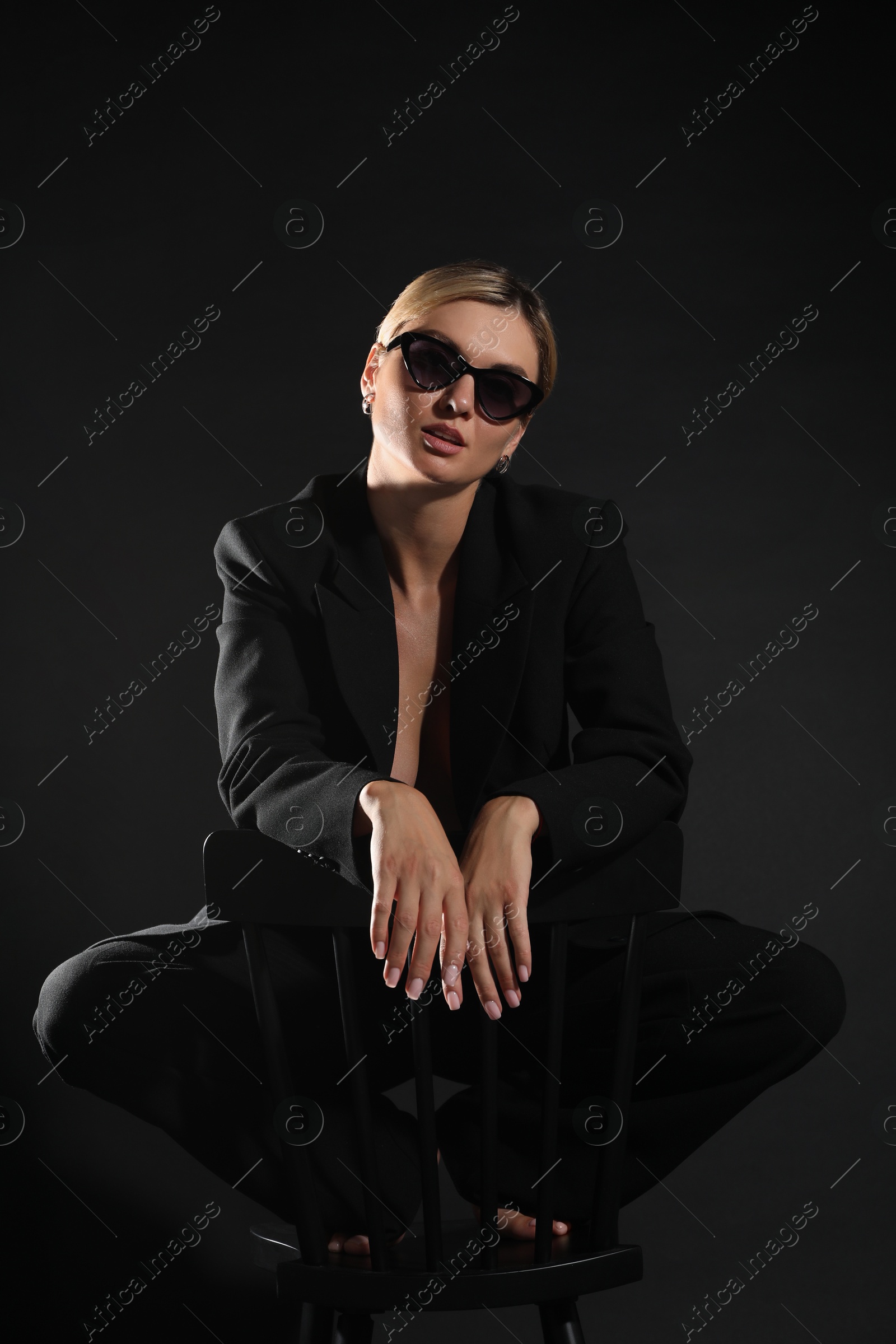 Photo of Beautiful woman in stylish suit on chair against black background