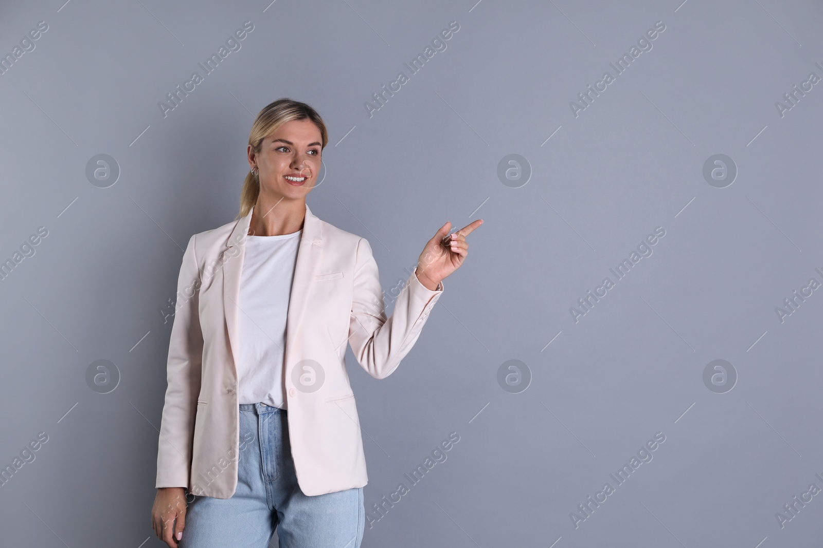 Photo of Beautiful woman in stylish jacket pointing at something on grey background, space for text