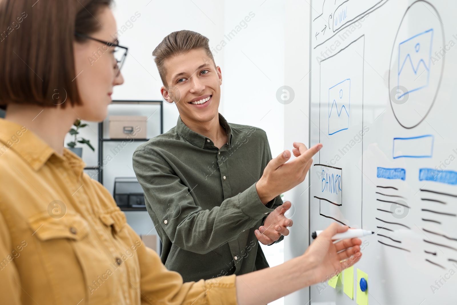 Photo of Developing UI design. Man and woman drawing website wireframe on whiteboard indoors