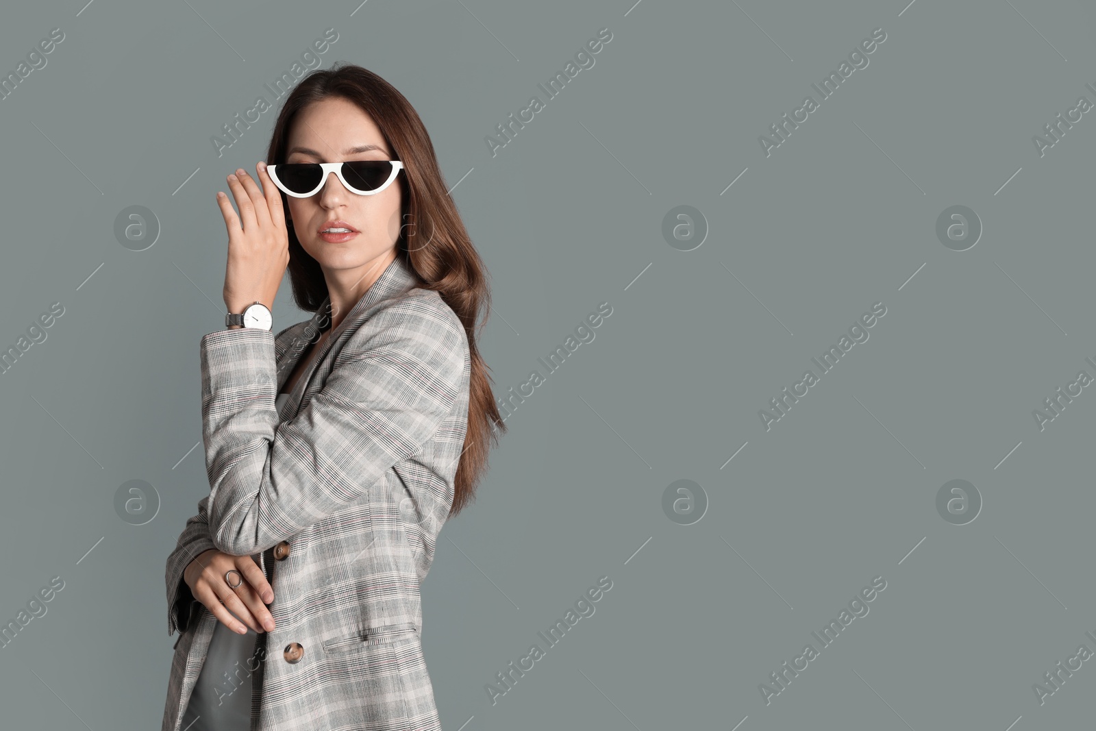 Photo of Beautiful woman with stylish jacket and sunglasses on grey background, space for text