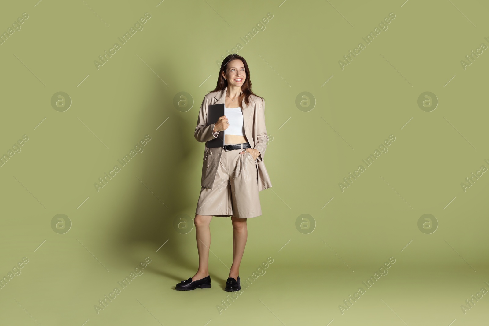 Photo of Beautiful woman in stylish beige suit with laptop on olive background