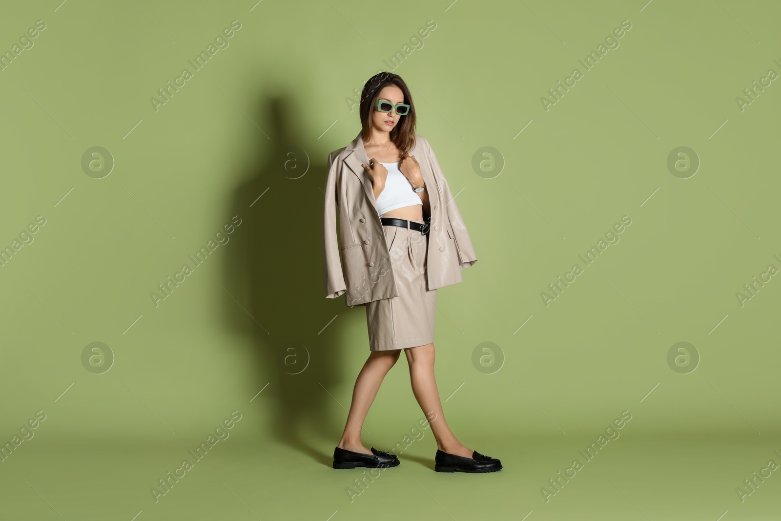 Photo of Beautiful woman in stylish beige suit and sunglasses on olive background