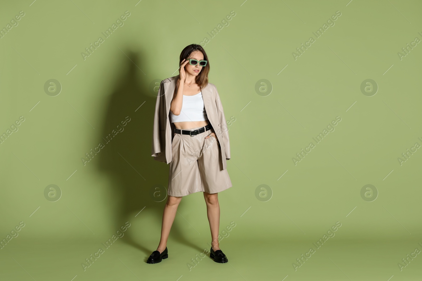 Photo of Beautiful woman in stylish beige suit and sunglasses on olive background