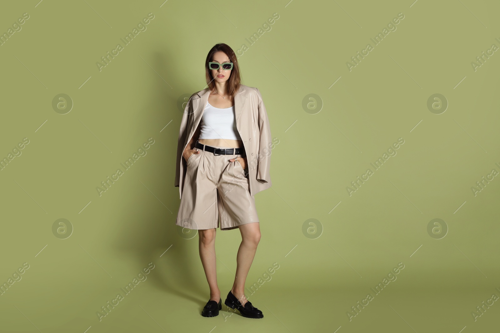 Photo of Beautiful woman in stylish beige suit and sunglasses on olive background, space for text