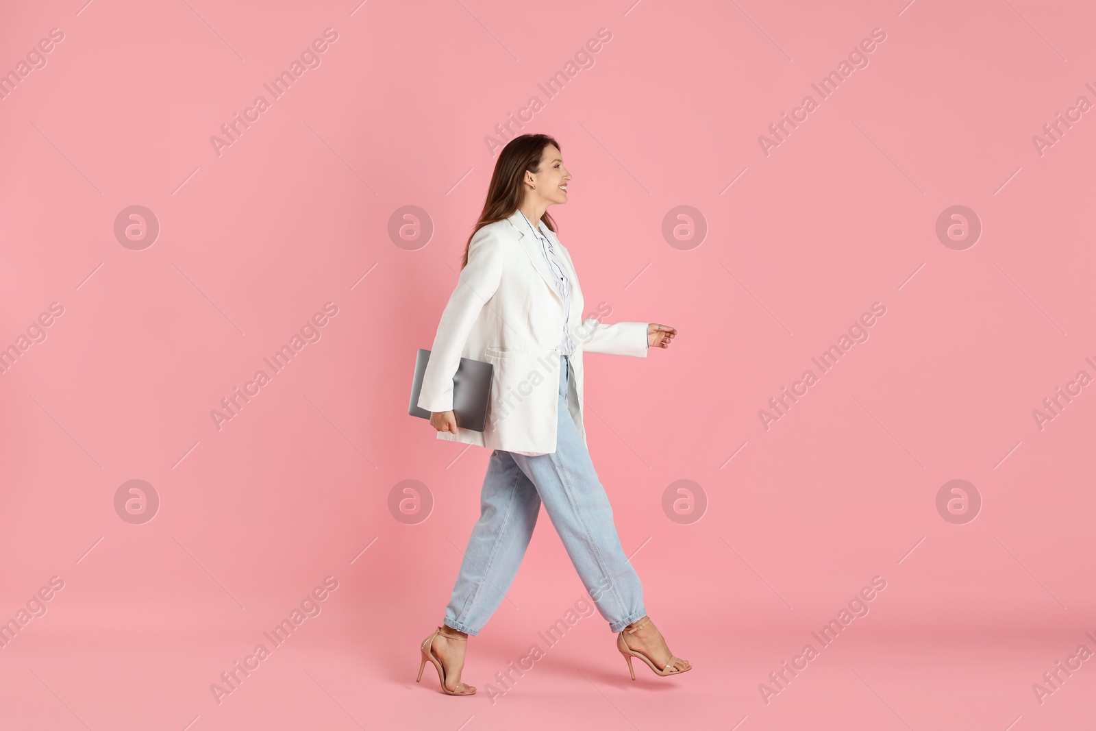 Photo of Beautiful woman in stylish white jacket with laptop on pink background