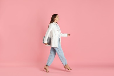 Beautiful woman in stylish white jacket with laptop on pink background