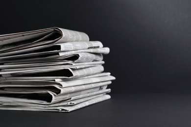 Stack of newspapers in different languages on black background. Space for text