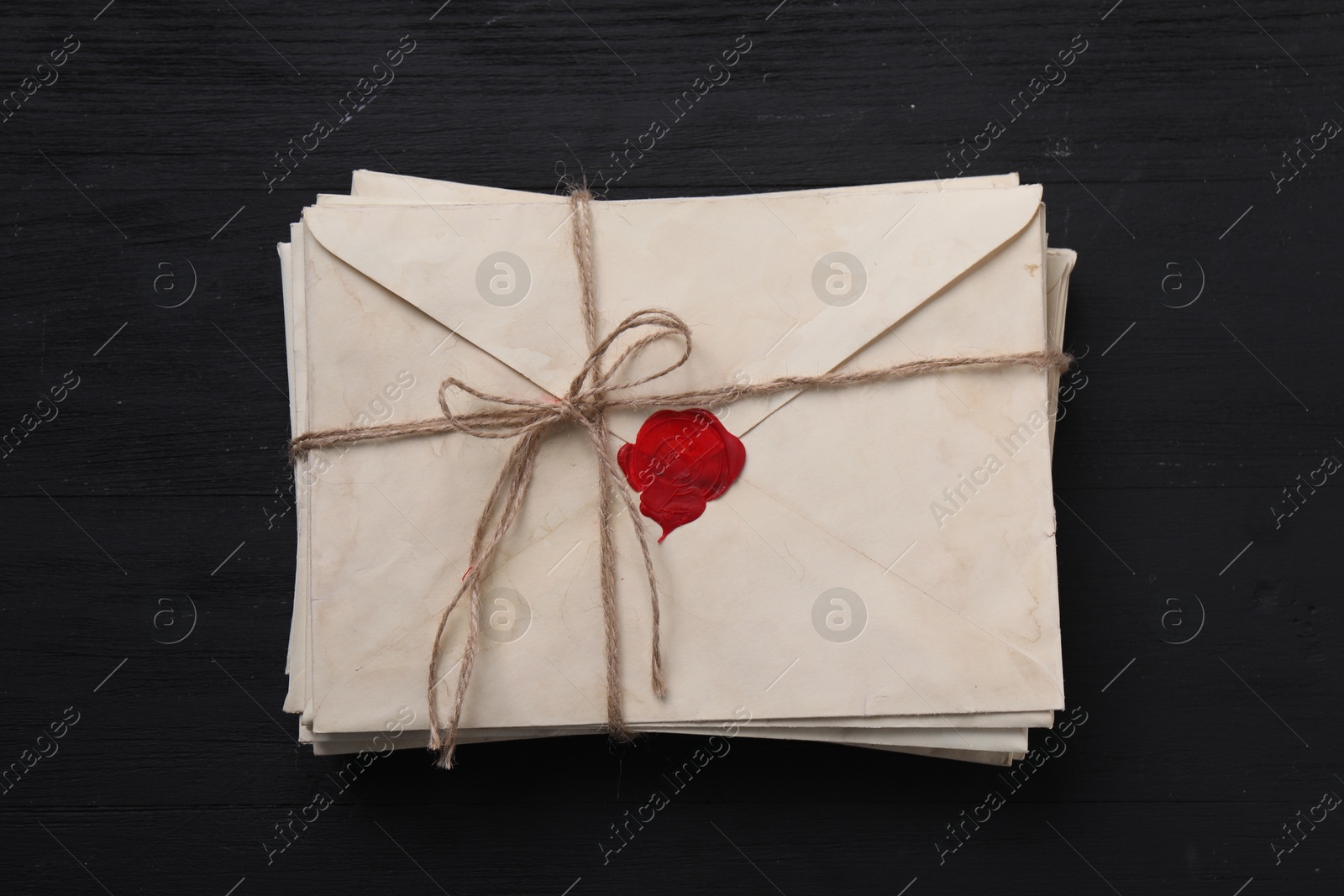 Photo of Stack of old letter envelopes tied with twine on black wooden table, top view