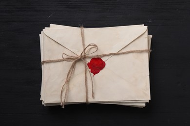 Stack of old letter envelopes tied with twine on black wooden table, top view