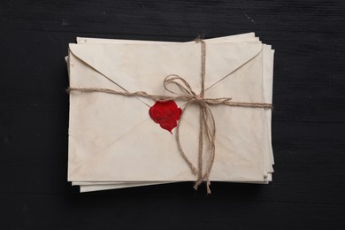 Stack of old letter envelopes tied with twine on black wooden table, top view