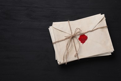 Photo of Stack of old letter envelopes tied with twine on black wooden table, top view. Space for text