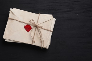 Photo of Stack of old letter envelopes tied with twine on black wooden table, top view. Space for text