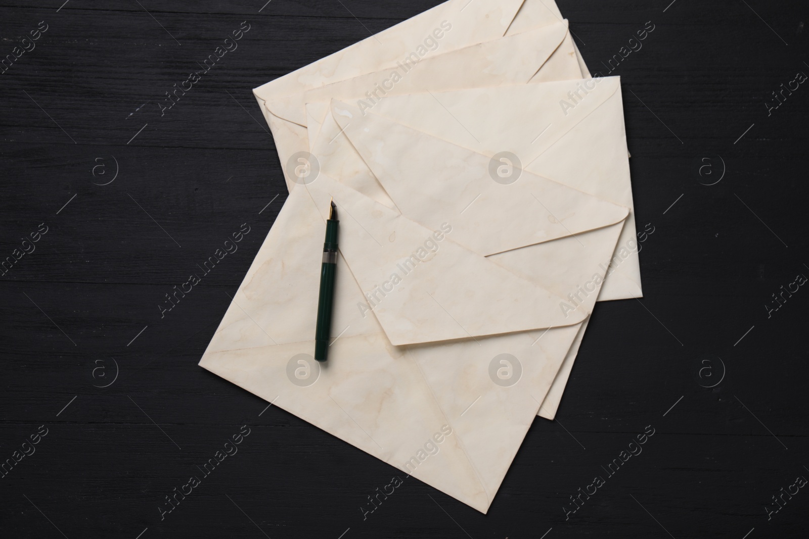 Photo of Old letter envelopes and fountain pen on black wooden table, top view