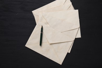 Photo of Old letter envelopes and fountain pen on black wooden table, top view