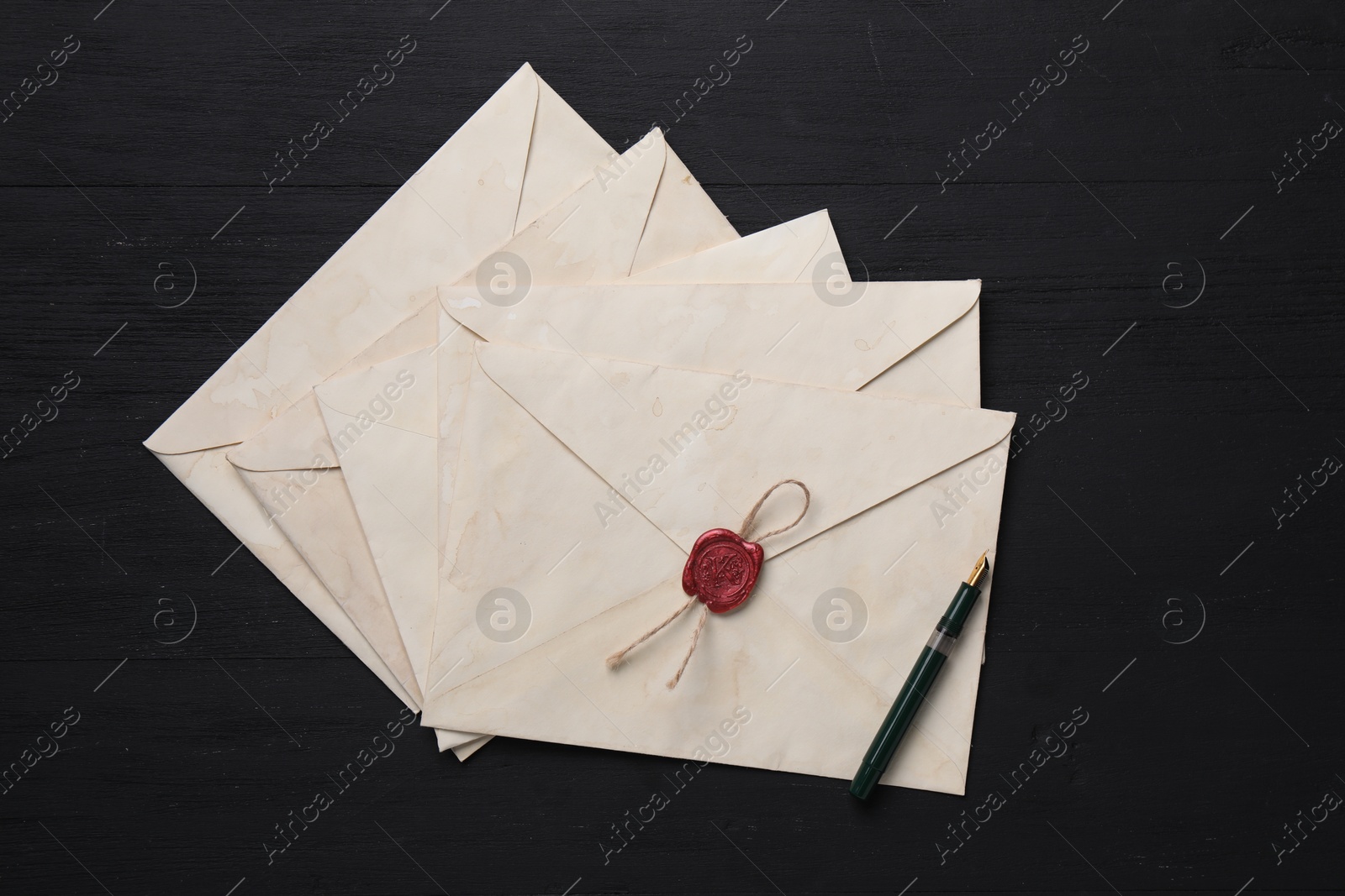 Photo of Old letter envelopes and fountain pen on black wooden table, top view