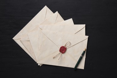 Old letter envelopes and fountain pen on black wooden table, top view