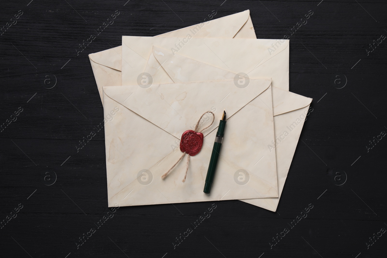 Photo of Old letter envelopes and fountain pen on black wooden table, top view