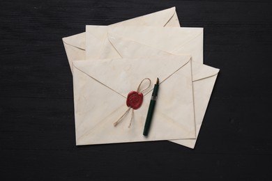 Old letter envelopes and fountain pen on black wooden table, top view