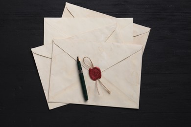 Old letter envelopes and fountain pen on black wooden table, top view