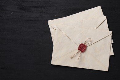 Old letter envelopes and fountain pen on black wooden table, top view