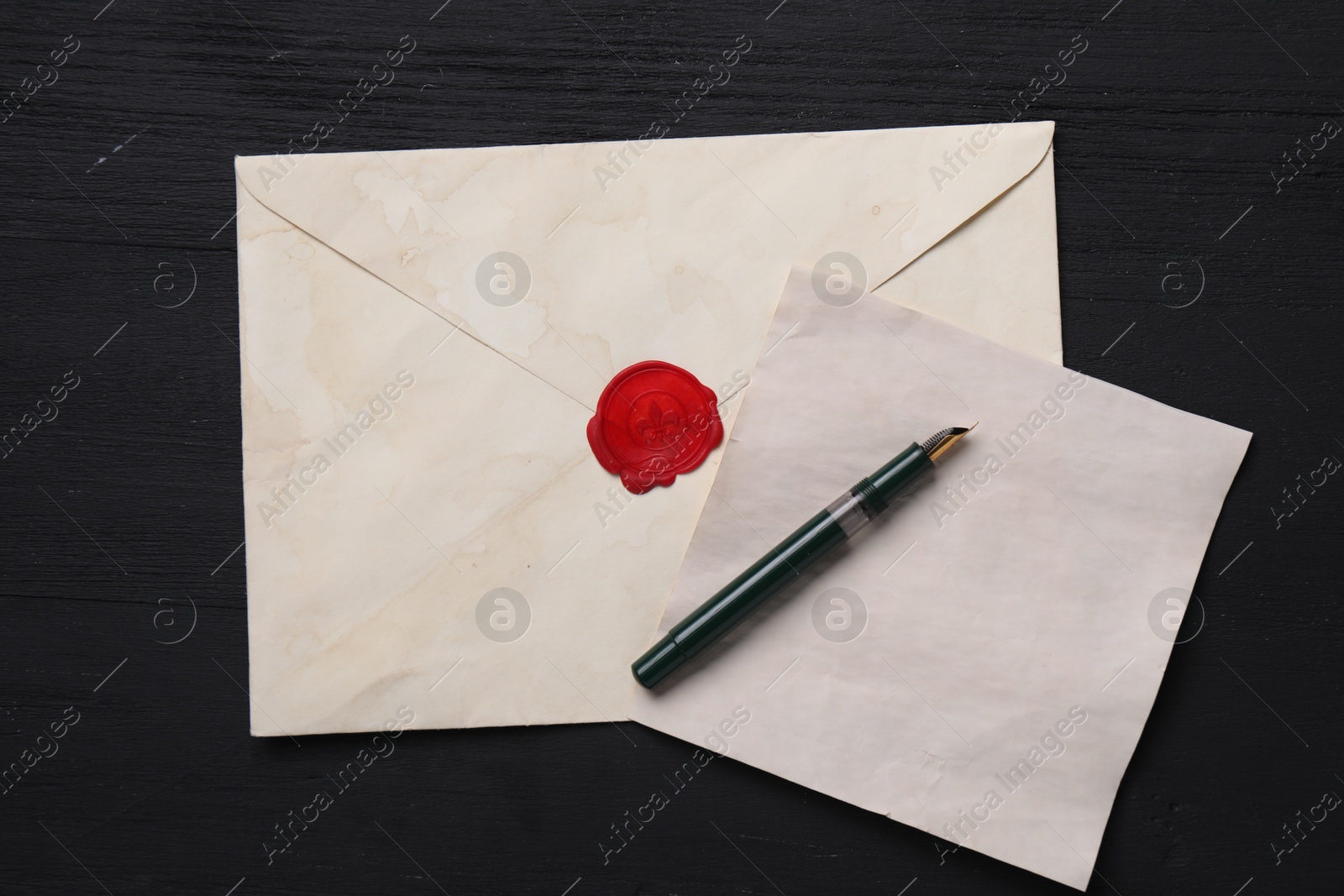 Photo of Old letter, envelope and fountain pen on black wooden table, top view