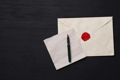 Old letter, envelope and fountain pen on black wooden table, top view. Space for text