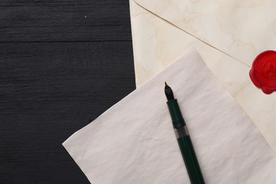 Photo of Old letter, envelope and fountain pen on black wooden table, top view