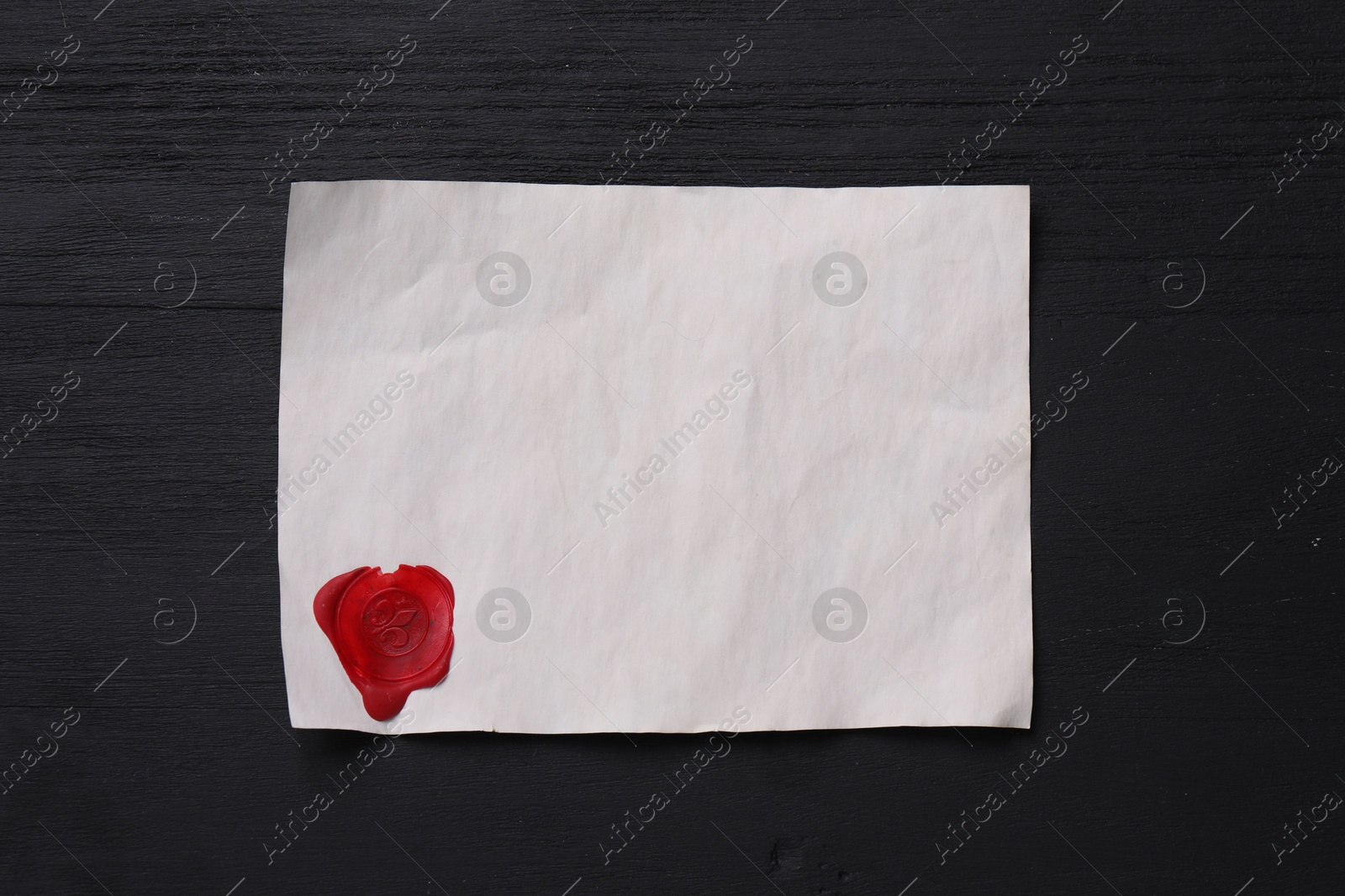 Photo of Blank old letter with wax stamp on black wooden table, top view