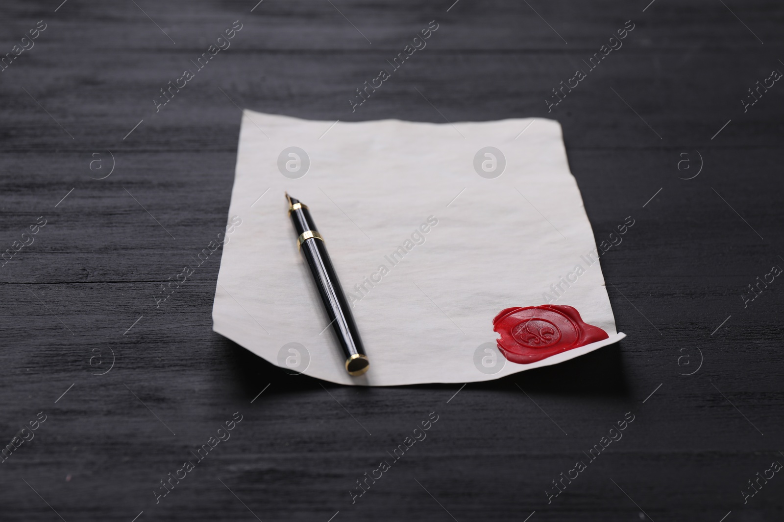 Photo of Old letter with wax stamp and fountain pen on black wooden table, closeup