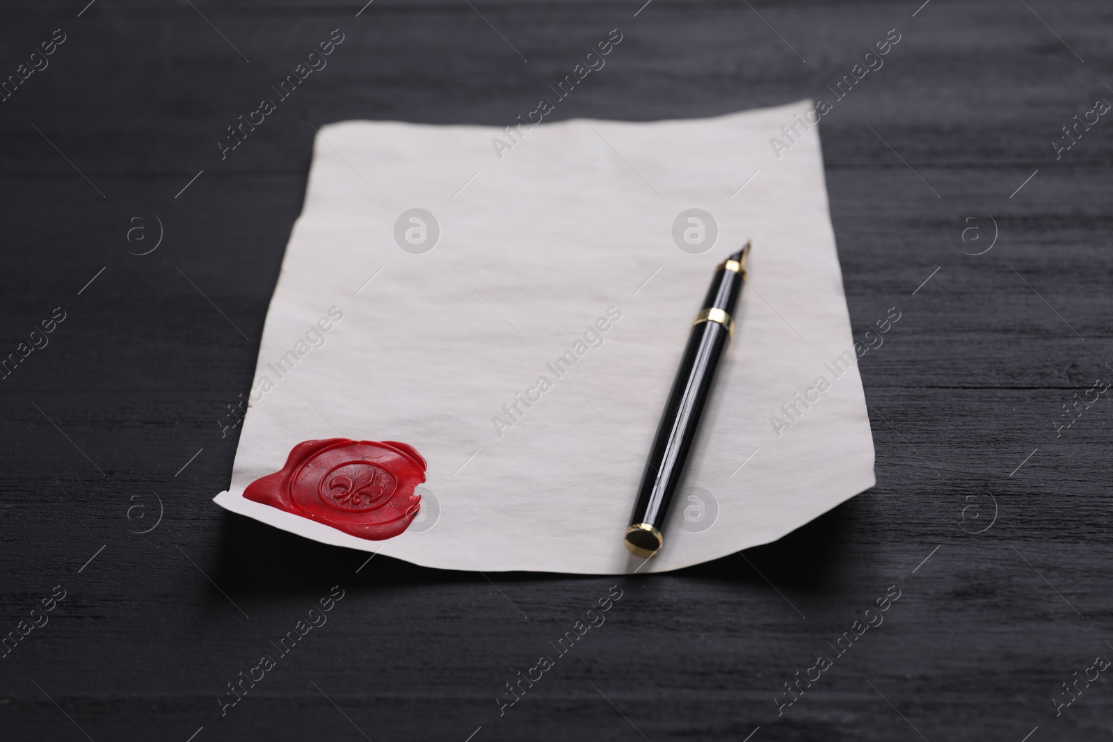 Photo of Old letter with wax stamp and fountain pen on black wooden table, closeup