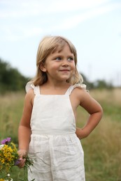 Cute little girl with flowers at meadow. Child enjoying beautiful nature