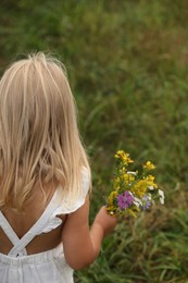 Photo of Little girl with meadow flowers outdoors, back view. Child enjoying beautiful nature