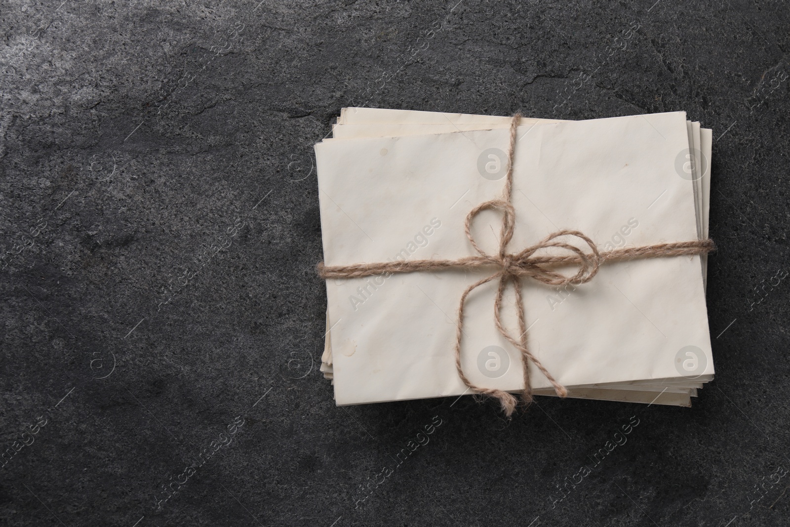 Photo of Stack of old letters tied with twine on grey table, top view. Space for text