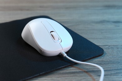 Photo of Computer mouse with mousepad on wooden table, closeup