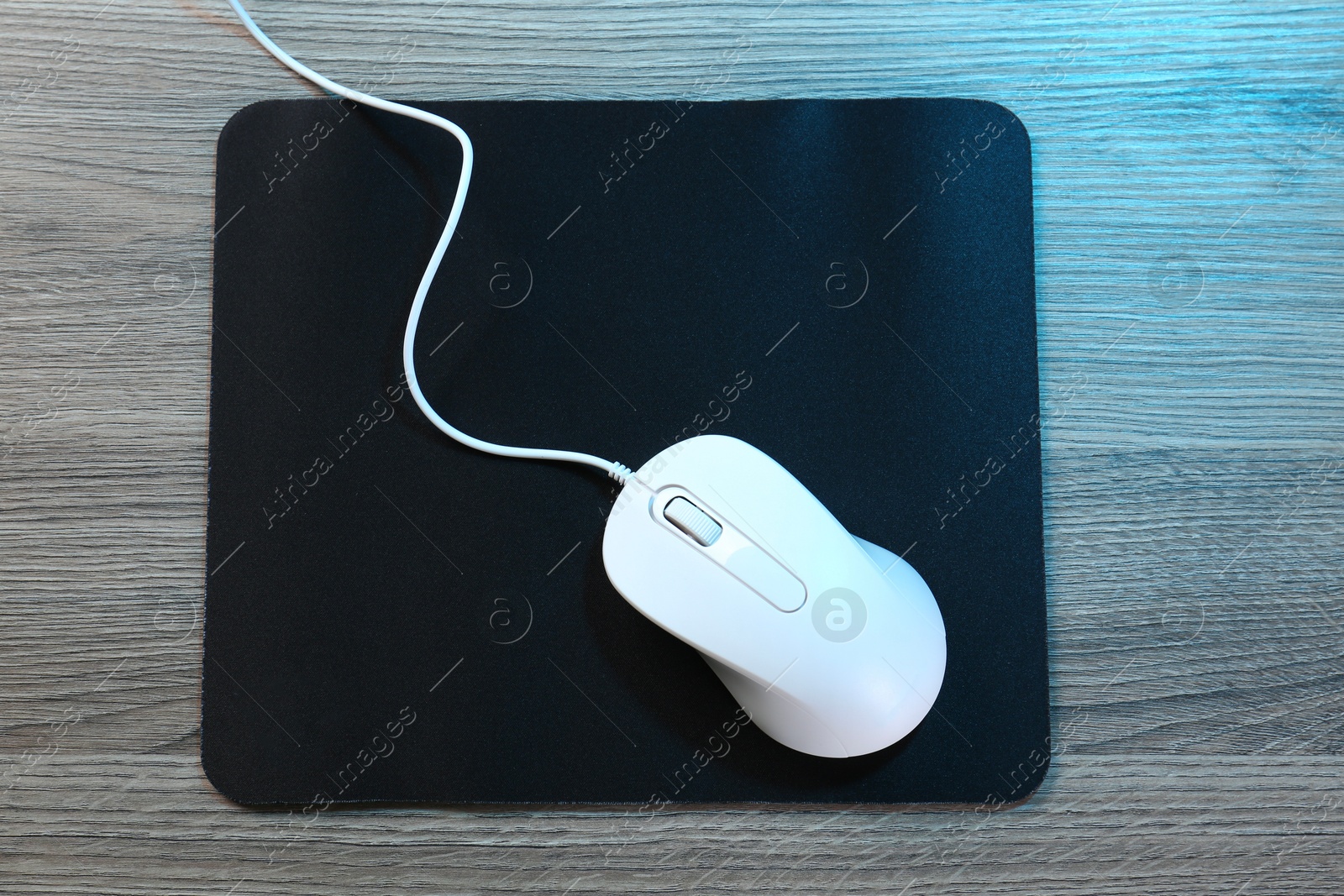 Photo of Computer mouse with mousepad on wooden table, top view